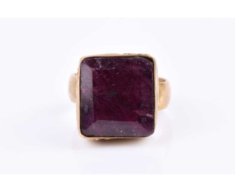 A yellow metal and corundum ring, set with a large rectangular-cut ruby (treated),1/5 x 1.4 cm, within a yellow metal bezel s