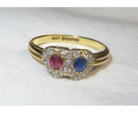 An 18ct. gold Dress Ring of entwined heart design, set with a ruby and sapphire and surrounded by small diamonds.