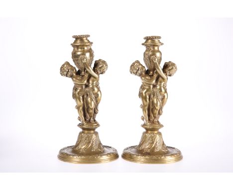 A PAIR OF FRENCH GILT-BRASS FIGURAL CANDLESTICKS, 19TH CENTURY, each stick with paired putti holding aloft an urn-form candle