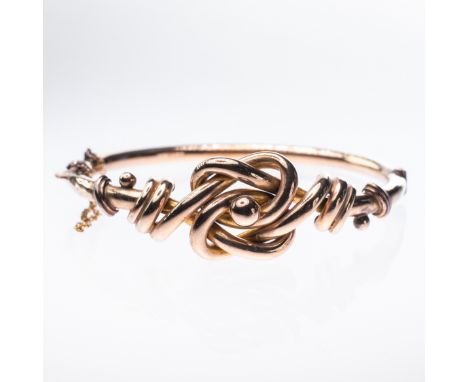A VICTORIAN 9CT YELLOW GOLD BANGLE, the large knot style mount, hinged with integral tongue clasp and safety chain. Stamped 9