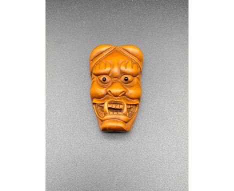 A Japanese hand carved Hannya mask netsuke. Designed with black bead eyes and signed. [5cm in length] 