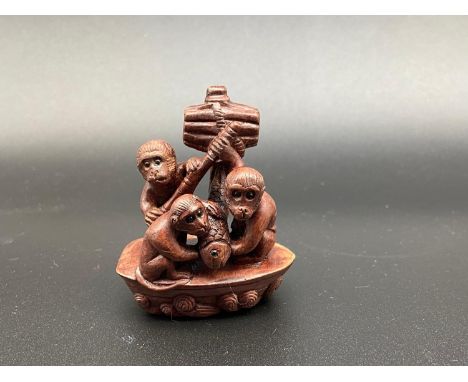 A Japanese hand carved netsuke of three monkey's on a sailing boat catching a koi carp. All designed with black bead eyes and