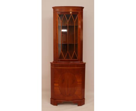 A bow-fronted yew veneered corner cabinet - with dentil cornice over an astragal glazed cupboard with two interior removable 