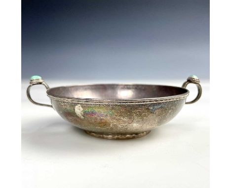 An eastern silver twin handled wine taster, the loop filigree handles set with a jade cabochon, the whole with repousse finis