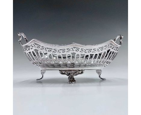 A George V silver basket by Harry Atkin, of oval section with twin cast scroll handles over the pierced body, raised on four 