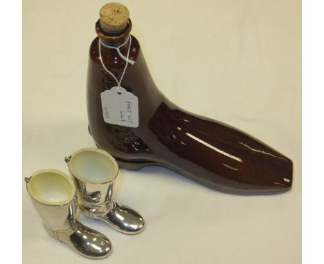 Two plated spirit cups in the form of riding boots, together with a treacle glazed pottery flask in the form of a boot 