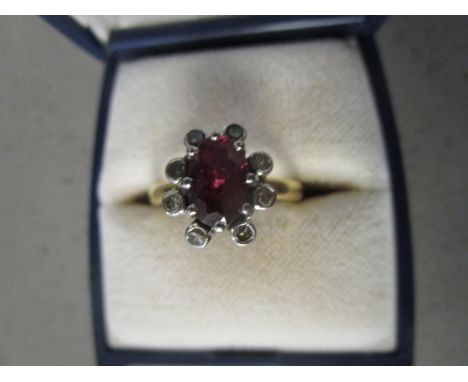 An 18ct yellow gold ruby and diamond cluster ring, claw set oval ruby surrounded by eight diamonds 