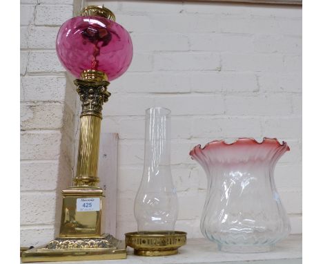 A Victorian style brass Corinthian column oil lamp with cranberry reservoir and shade