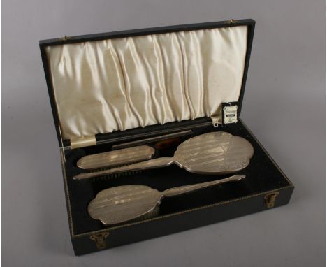 A four piece silver backed dressing table set with engine turned and engraved decoration comprising a hand brush, mirror, com