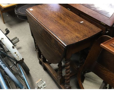 An oak gate leg drop leaf table with barley twist supports.