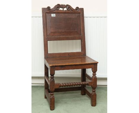A late 18th century English oak vernacular chair with a carved top rail panel back and seat and bobbin turned supports.