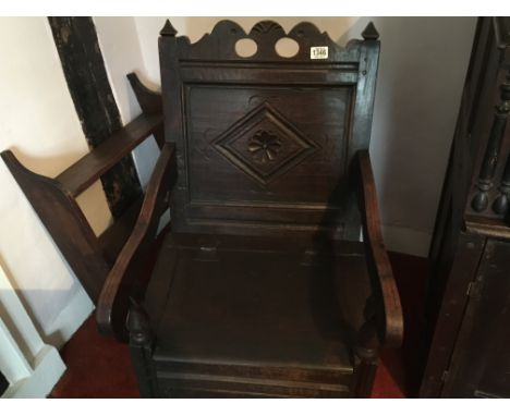 An Early 18th century English oak vernacular commode chair with a carved panel back and open scroll arms
