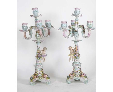 A pair of Sitzendorf porcelain three branch table candelabra, each profusely floral encrusted, mounted with putti, blue under