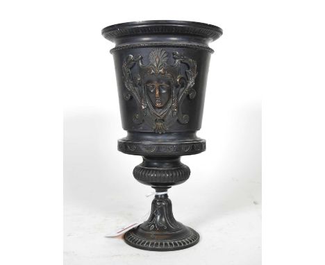 A 19th century bronze urn, having applied mask decoration, on gadrooned domed foot, height 22.5cm