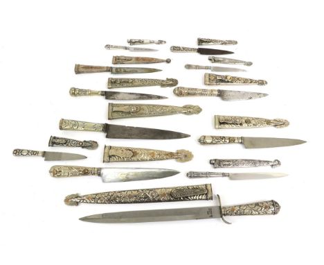 A Collection of Twelve Argentinian Gaucho Knives, of varying sizes, each with white metal hilt and scabbard elaborately embos