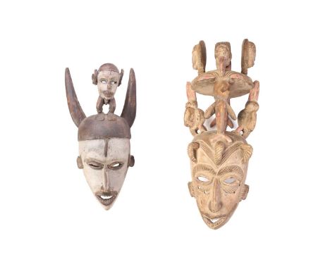Two Igbo carved wood masks, Nigeria, the larger mask carved from a single trunk, with birds, face masks and stylised crocodil