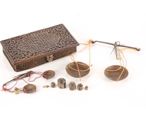 An Eastern coin scale in a fitted teak case carved with Islamic script, with two beams and pans in sizes and corresponding ir