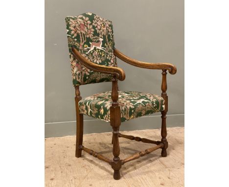 A Carolean style oak armchair, upholstered in tapestry fabric depicting a hunting scene, with scrolled arms and raised on tur