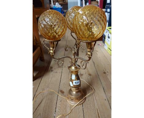 A vintage brass three branch table lamp with ceramic bosses, depicting hunting scenes and three diamond pattern moulded globe