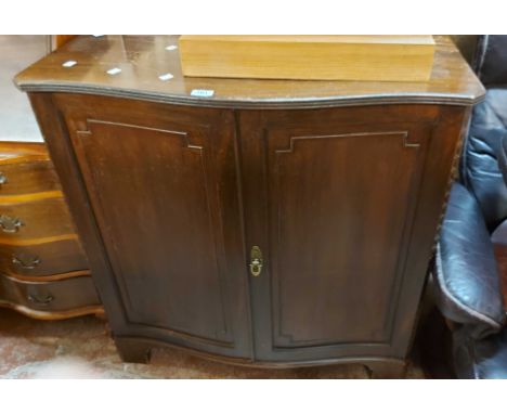 A 91cm vintage Maple &amp; Co. mahogany serpentine front cabinet with shelves enclosed by a pair of panelled doors, set on br