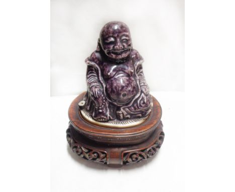 A small antique Chinese porcelain seated Buddha with purple glaze, set on a hardwood stand with pierced scroll decoration - m