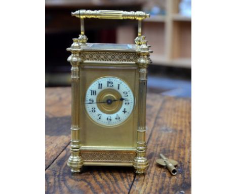 A gilt brass carriage clock with blind-fret tracery friezes and fluted pilaster pillars, gilt dial with enamelled chapter rin