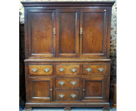 An 18th century jointed oak housekeepers cabinet having a pair of fielded panel doors flanking a fixed centre panel over thre
