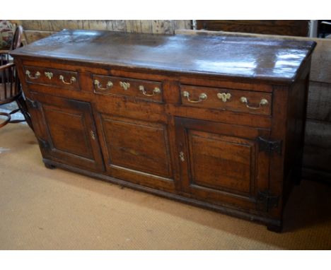 An 18th century oak low dresser, the moulded edge top over three drawers over a fielded centre panel, flanked by cupboards, o