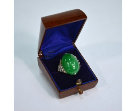 An Edwardian oval green jade cabochon ring, having six eight-cut diamonds on each shoulder, in white metal setting, in bakeli