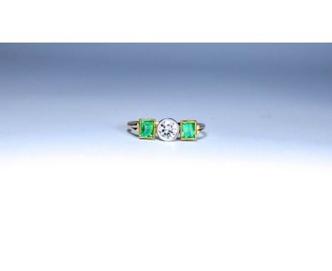 Art deco emerald and diamond ring, with a brilliant cut circular diamond to the centre flanked each side with a trap cut emer