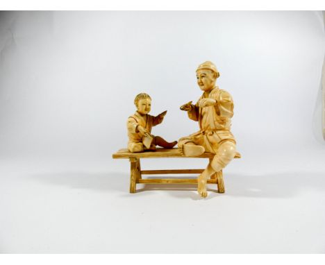 A Meiji period carved ivory figure group of father and child seated on a bench, red character marks to base. Height 13cms 