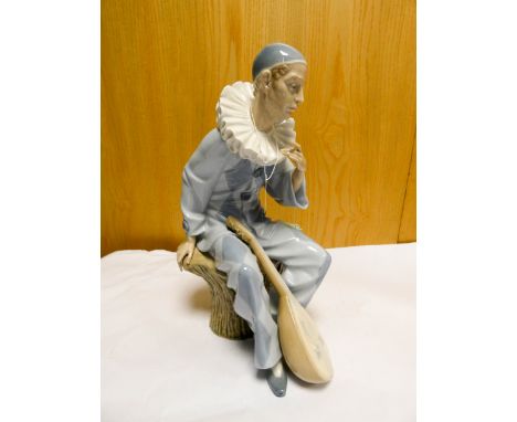 A Nao porcelain figurine of a Harlequin musician seated on a stump   Loss to fingers 