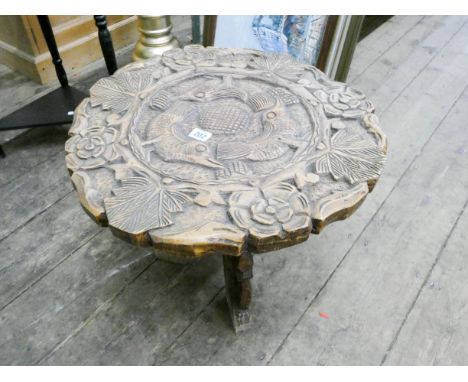 A highly carved wood coffee table on a folding tripod base 