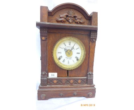 Carved oak hooded cased mantel clock ex. Fattorini &amp; Sons of Bradford, the circular brass and enamel dial painted roman n