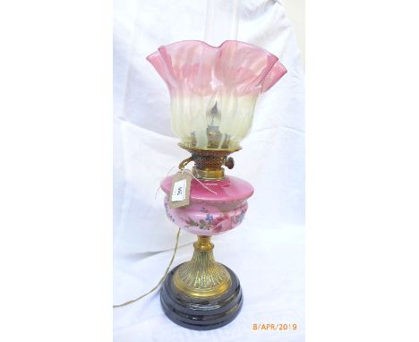 A converted Victorian oil lamp on fluted brass base on circular ebonised plinth, part cranberry glass shade and pink bowl wit