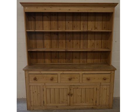 A large stripped pine kitchen dresser, the plate rack with two open shelves on a base with three drawers and panelled cupboar