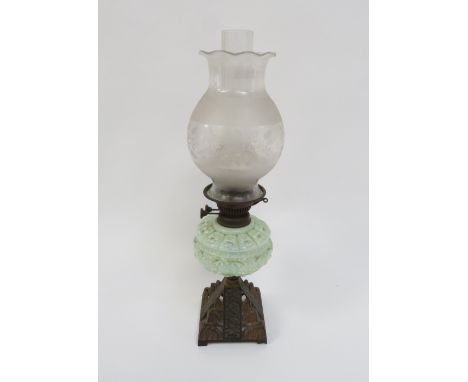 An early 20th Century oil lamp with a stepped cast metal base, milk glass reservoir and glass shade, 58cm high