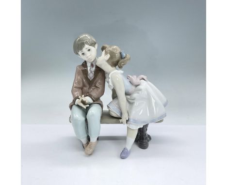 Glazed porcelain figural of a girl about to kiss a boy on the cheek as they both sit on a bench. Lladro backstamp. Issued: 19