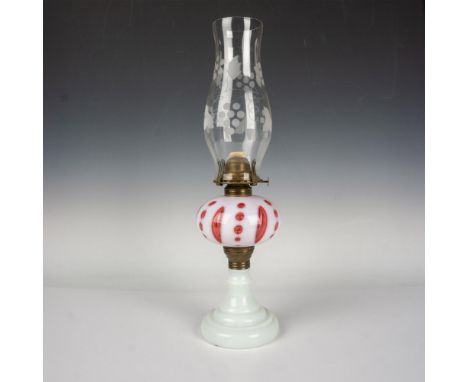 A white milk glass oil lamp body with a cranberry-red and white glass orb in the center. Includes a clear glass lamp shade de