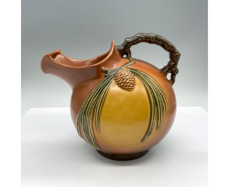 A round art pottery of a pitcher in the Pine Cone patter. The handle is formed as a the branch of the pine tree. Roseville 13