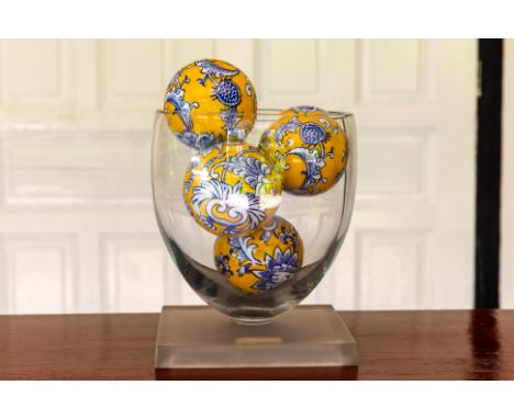 A GLASS VASE WITH CERAMIC BALLS
An oval shaped glass vase with a square base, the ceramic balls decorated with blue floral mo