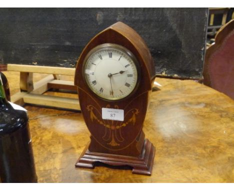 An early 20th century inlaid mahogany mantle clock, the shaped lancet case with stylised foliate and swag inlay, white enamel