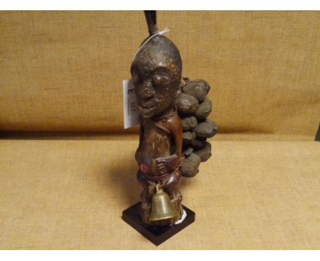 An African carved wooden tribal figure, possibly Congo, the head with horn surmount, bearing pods and with bell to waist, on 