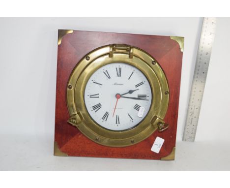 MARINE CLOCK FORMED AS A PORTHOLE MOUNTED ON A MAHOGANY BACK PLATE, APPROX 30CM SQUARE