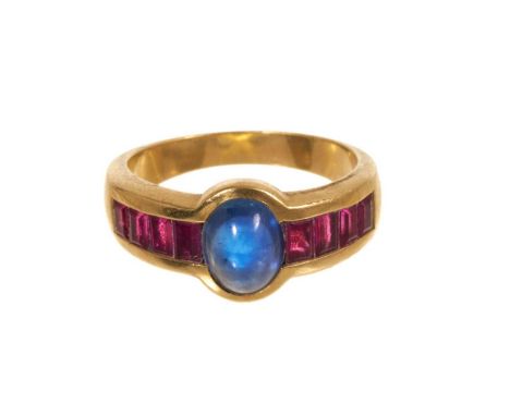 Sapphire and ruby ring with a central oval blue sapphire cabochon with eight rectangular step cut rubies to the shoulders in 