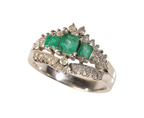 AN EMERALD AND DIAMOND DRESS RINGin 18ct white gold, set centrally with three graduating step cut emeralds totalling c.0.70 c