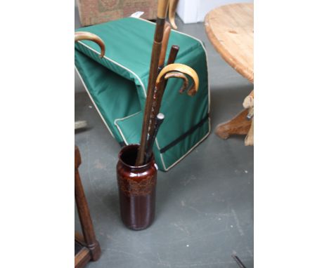 A stone glazed umbrella stand with a selection of walking sticks including snake head carved stick set with glass eyes, toget