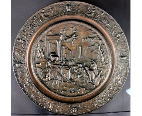 A cast iron charger, decorated with a scene of maidens playing musical instruments in a Greek city, 39.5cm