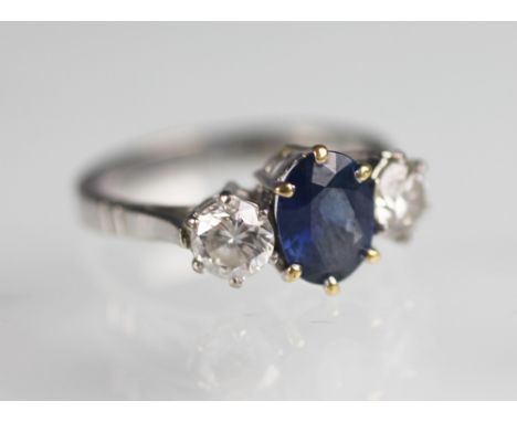 A sapphire and diamond three stone ring, the central oval sapphire flanked by a brilliant cut diamond to either side (each me