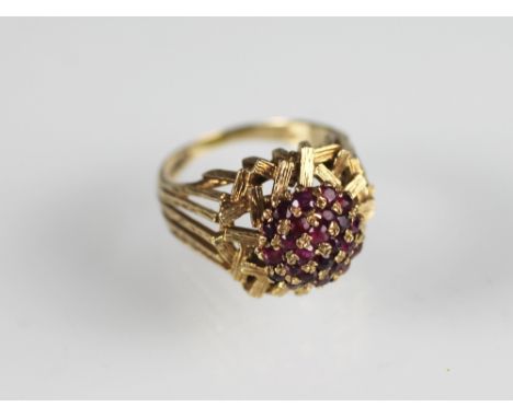 A 9ct yellow gold and ruby set dress ring, London 1974, the abstract gold ring set with a central convex, circular panel of r
